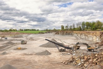 Excavator at a stone crusher with a conveyor in a limestone quarry with a waiting truck in a rural