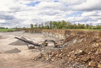 Excavator at a stone crusher with a conveyor in a quarry in a the countryside
