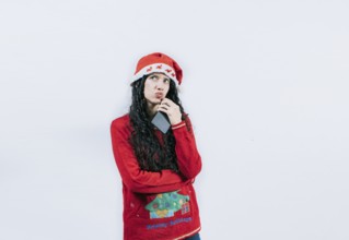 Young woman in christmas sweater thoughtful holding cell phone isolated. Girl in christmas hat