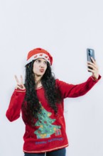 Funny latin girl in Christmas hat taking selfies and making gestures isolated. Cheerful young woman