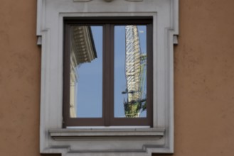 Window of a building with a reflection of a construction crane in the city of Rome, Italy