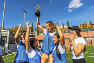 Happy young women soccer players celebrating victory on a sunny outdoor field, lifting the