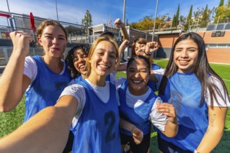 Group of smiling young women players celebrating success and victory on a soccer field, posing for