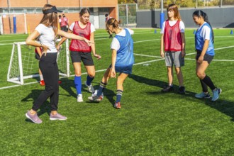 Female coach instructing a diverse group of young women soccer players on a green artificial turf