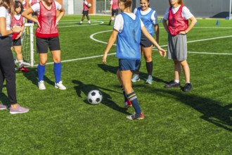 Diverse women soccer players training together on a sunny outdoor turf field, practicing dribbling,