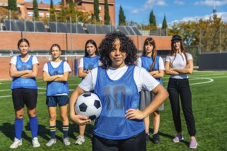 Diverse group of young women, wearing blue vests and sportswear, standing proudly on a green