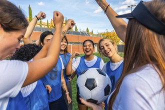 Happy female soccer team players huddling together on the field, raising their fists in