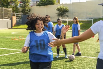Young female soccer player high fiving her coach on a green artificial turf field, training with