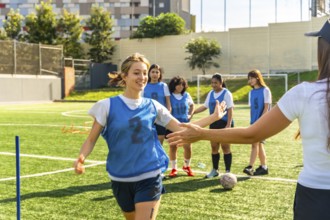 Young female soccer player in a blue bib high fiving her coach on a green artificial turf field,