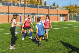 Girls soccer team receiving instructions from their female coach while practicing ball control and
