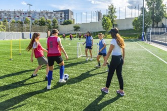 Female soccer teammates training on a sunny artificial turf field, practicing dribbling, passing