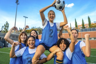 Group of diverse women soccer players cheering and lifting a teammate with a soccer ball on a green