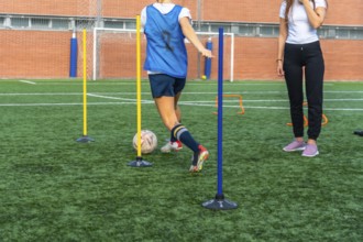 Young woman in a blue bib practicing soccer dribbling skills, maneuvering a ball through training