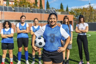 Diverse women's soccer team, featuring a smiling player holding a football, standing proudly on a