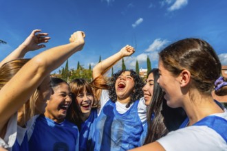 Young women soccer players cheering with arms raised in celebration, smiling and embracing after