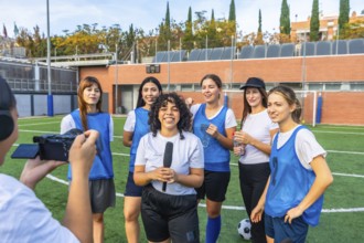 Female football players and their coach standing on a green field after a game, giving an interview