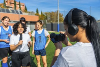 Videographer with headphones filming a reporter holding a microphone and interviewing a group of