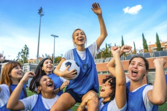 Joyful female soccer players lifting a teammate with the ball overhead, celebrating a win together