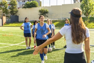 Young women's soccer team participating in a training session on a sunny artificial turf field,