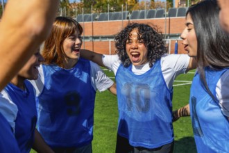 Young diverse women football players joining arms in a huddle, enthusiastically celebrating a