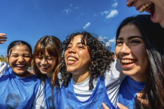 Diverse group of young girls standing close, smiling and laughing under a bright blue sky,