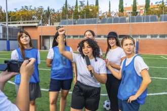 Happy young women's soccer team and coach giving an interview on artificial turf field, celebrating