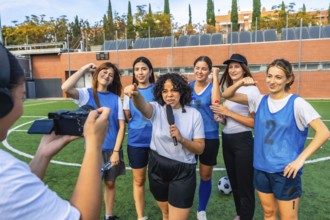 Reporter with microphone interviewing a diverse women's soccer team on a green field, capturing