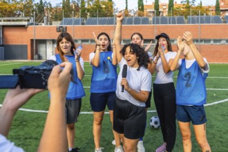 Women's football team standing on grass field, cheering and celebrating a win as one player holds a