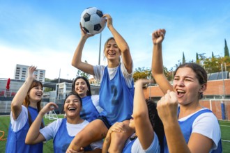 Young happy women soccer team players celebrating victory, one player is sitting on teammates'