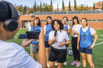 Female sports journalist interviewing a diverse women's soccer team on a green field, capturing
