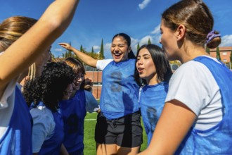 Group of diverse women's soccer players huddling on the field, actively celebrating their success