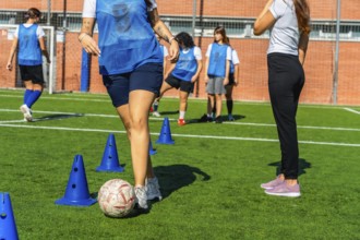 Young women's soccer team practicing dribbling drills with cones on green turf, focused and