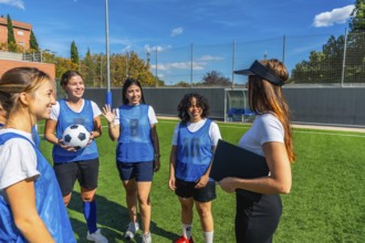 Women soccer players in blue pinnies listening attentively to their female coach explaining