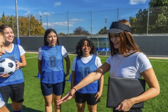 Coach, wearing a visor and holding a folder, explaining strategy to a smiling female soccer team on
