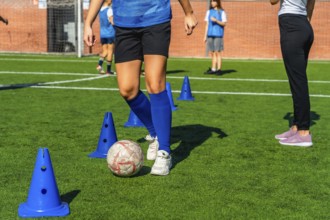 Young girl in a blue jersey practicing soccer dribbling skills around orange cones on a green