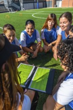 Women's soccer team members sitting on artificial grass, carefully analyzing game tactics and