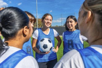 Women soccer players in blue uniforms huddled on a green field, smiling and planning strategy