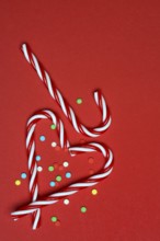 Candy canes and sugar confetti against red background, Christmas