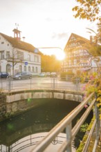 Bridge over a river, half-timbered buildings at sunset, autumn trees next to the road, Aidlingen,