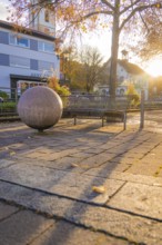 Bench next to a big ball, long shadows at sunset, autumnal town square, Aidlingen, Böblingen