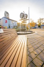 Municipal square with church and sculpture at sunset, concrete paving and autumn trees, Aidlingen,