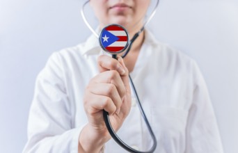 Female doctor holding stethoscope with Puerto Rico flag. National health system of Puerto Rico