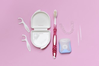 Top view of dental clear aligners, toothbrush, toothpicks and floss on pink background with copy