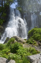 A waterfall flows over rocks surrounded by lush green vegetation in summer, Shaki Waterfall, Syunik