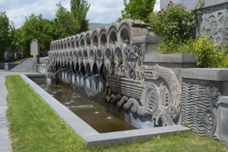 Stone fountain with sculptures surrounded by plants in bright weather, monument to the 40th