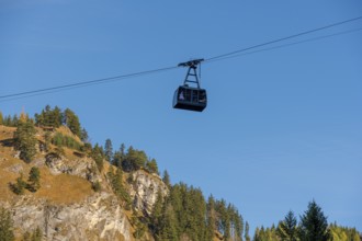 A Tegelbergbahn cabin floats over a mountainous landscape under a clear blue sky, near Schwangau,