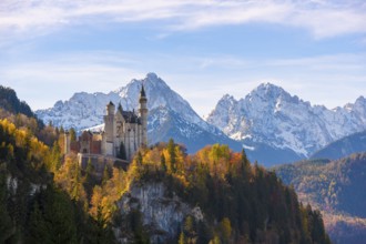 Neuschwanstein Castle stands majestically on a hill with autumn trees, surrounded by snow-capped