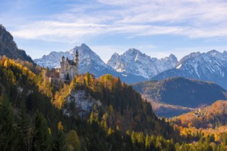 Neuschwanstein Castle in a forest of colorful autumn trees, against snow-covered mountains and blue
