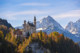 Neuschwanstein Castle rises impressively against a snowy mountain backdrop, surrounded by autumnal