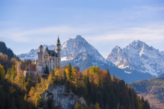 Neuschwanstein towers over an autumnal valley and magnificent snow-covered mountain formations,